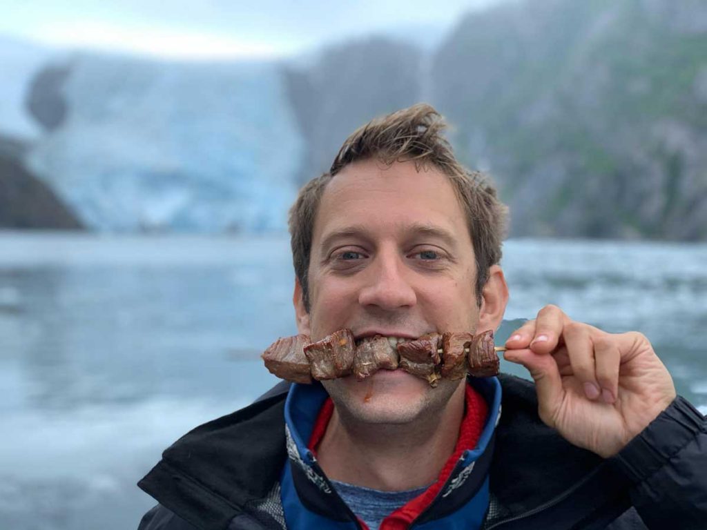 Mike Still enjoying a snack against a backdrop of a glacier in Alaska