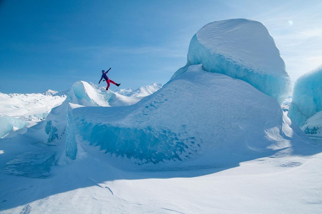 a person leaps between big blue ice formations at the Knik Glacier in Alaska