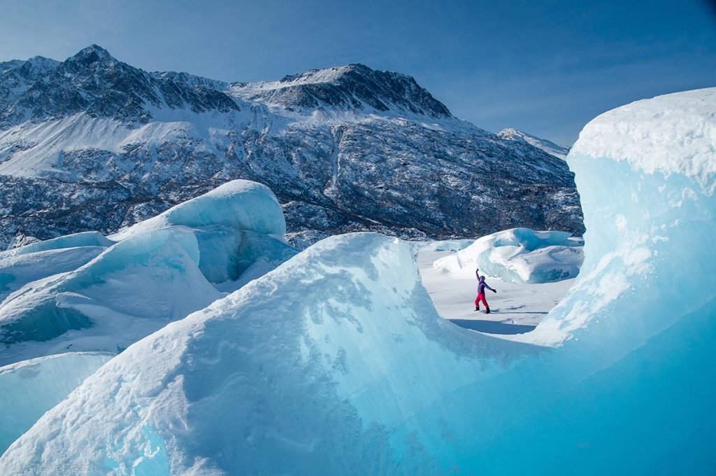 a person exploring the vibrant blue ice formations of the Knik Glacier