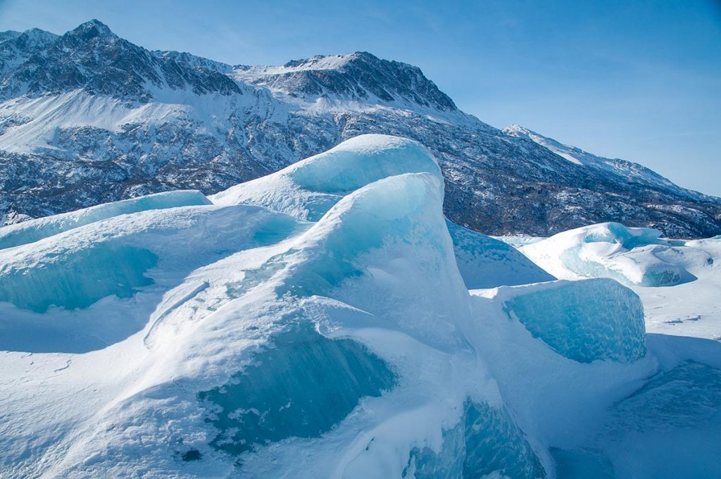 massive vibrant blue iceberg frozen into a lake in front of a snow-covered mountain ridge at Knik Glacier, Alaska