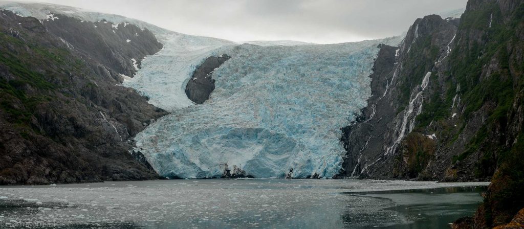 A massive blue and white tidewater glacier sits between two rocky mountains