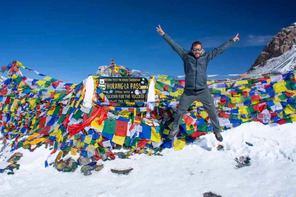 Mike Still posing at Thorong La Pass welcome sign with colorful prayer flags